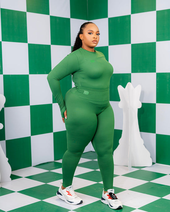 Model wearing the Evergreen Active Set, a green long-sleeve top and matching high-waisted leggings, against a green-and-white checkerboard backdrop.